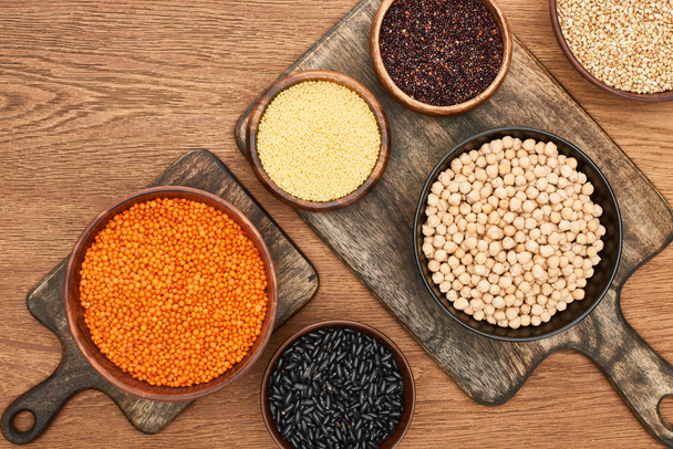 top view of bowls with beans, couscous, chickpea, red lentil and quinoa on wooden surface - Foto, afbeelding