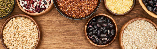 panoramic shot of bowls with oatmeal, buckwheat, beans and couscous on wooden surface - Photo, Image