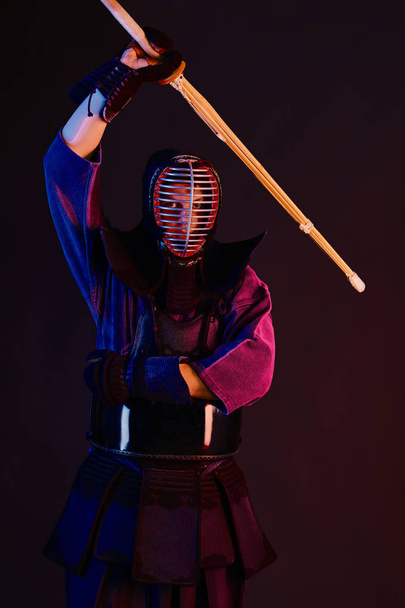 Primer plano, luchador Kendo con armadura, kimono tradicional, casco practicando arte marcial con espada de bambú shinai, fondo negro
. - Foto, Imagen