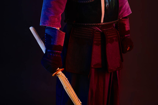 Primer plano, luchador Kendo usando una armadura, kimono tradicional está practicando arte marcial con espada de bambú shinai, fondo negro
. - Foto, imagen