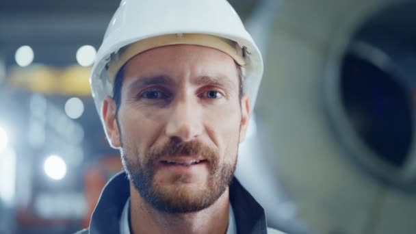Portrait of Smiling Professional Heavy Industry Engineer / Worker Wearing Safety Uniform and Hard Hat. In the Background Unfocused Large Industrial Factory - Πλάνα, βίντεο