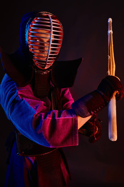 Close-up schot, Kendo vechter dragen in een harnas, traditionele kimono, helm beoefenen van krijgskunst met shinai bamboe zwaard, zwarte achtergrond. - Foto, afbeelding