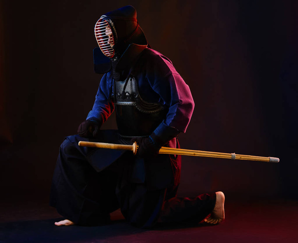 Close up shot, Kendo fighter wearing in an armor, traditional kimono, helmet practicing martial art with shinai bamboo sword, black background. - Zdjęcie, obraz