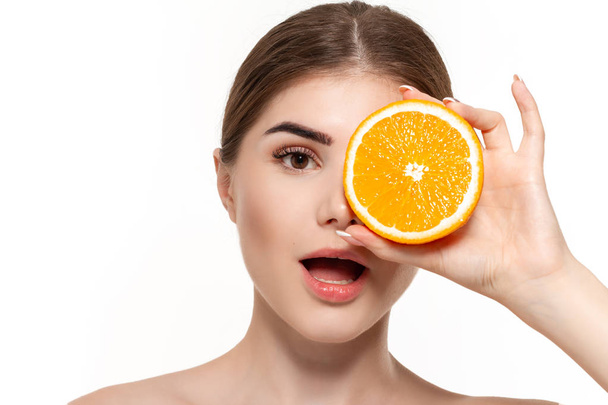 Retrato de cerca de una joven hermosa y feliz sosteniendo la mitad de las naranjas cerca de la cara aislada sobre fondo blanco. Concepto de belleza y salud
. - Foto, imagen