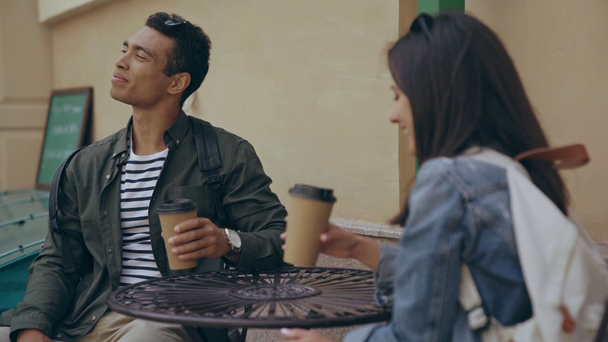 interracial couple sitting, talking and drinking coffee - Materiał filmowy, wideo