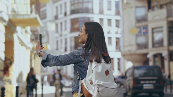 Kobieta z plecakiem ma czat wideo na ulicy - Materiał filmowy, wideo
