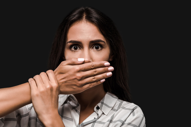 scared woman covering mouth while looking at camera isolated on black  - Photo, Image
