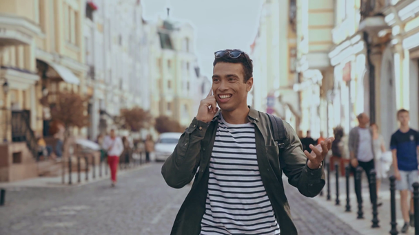 KYIV, UKRAINE - JULY 9, 2019: bi-racial man walking at street and talking on smartphone - Video