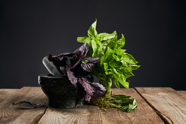 mortar with fresh green and purple basil with rosemary on wooden table isolated on black - 写真・画像