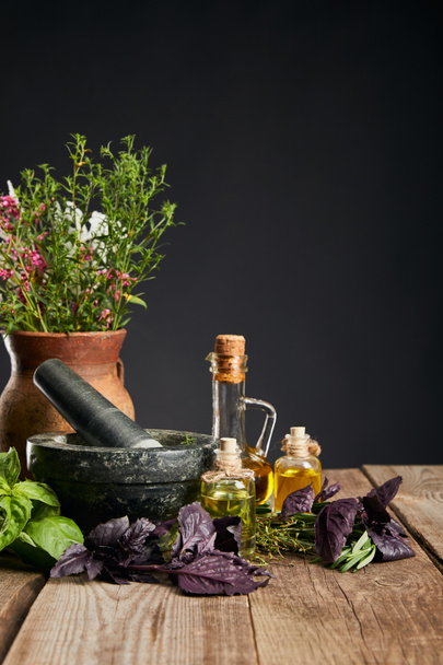 grey mortar near clay vase with herbs on wooden table isolated on black - Zdjęcie, obraz