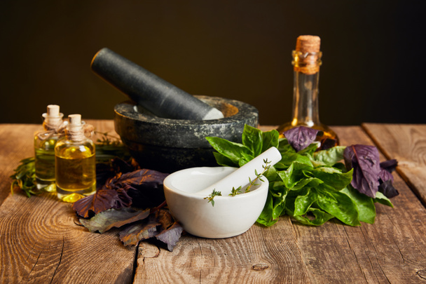 mortars with pestles and bottles near fresh herbs on wooden table isolated on black - Foto, Imagen