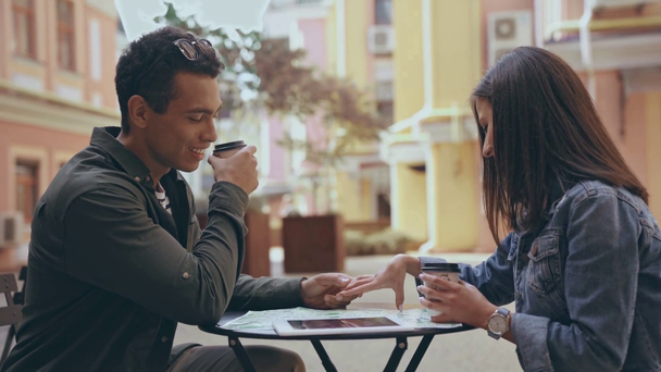 interracial couple sitting, holding hands and drinking coffee - Materiał filmowy, wideo