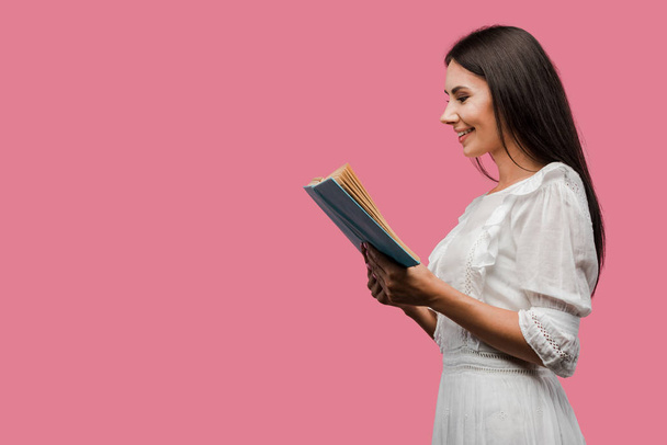 cheerful woman in dress reading book isolated on pink  - Fotó, kép