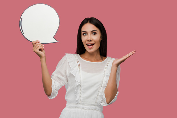 surprised young woman holding blank speech bubble and gesturing isolated on pink  - Фото, зображення