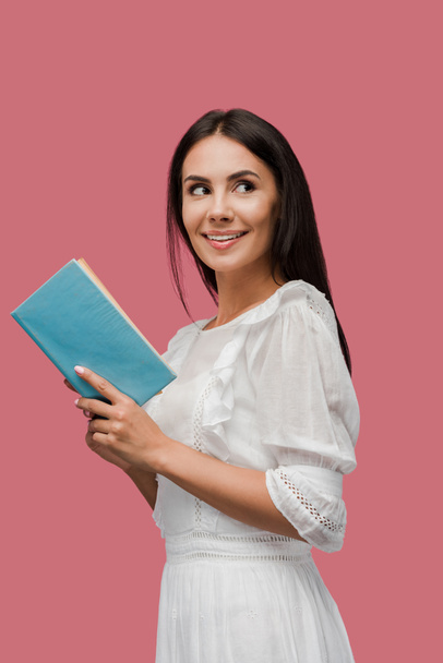 cheerful young woman in dress holding book isolated on pink  - Photo, Image
