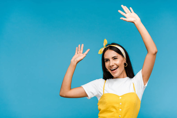 happy young woman in headband gesturing isolated on blue  - Foto, afbeelding