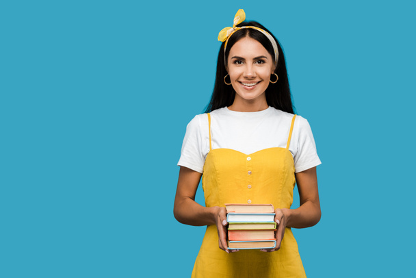 happy girl holding books and looking at camera isolated on blue  - Foto, Imagem
