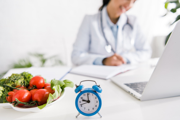 cropped view of nutritionist near vegetables and alarm clock  - Photo, Image