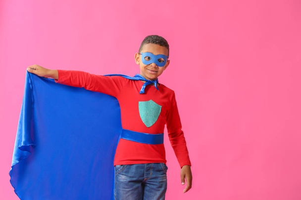 色の背景にスーパーヒーローの服を着たかわいいアフリカ系アメリカ人の少年 - 写真・画像