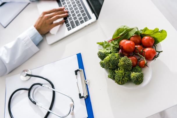 selective focus of vegetables near doctor typing on laptop  - Photo, Image