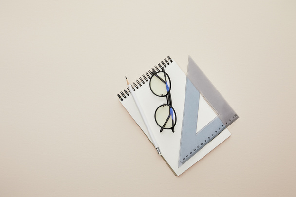 felső nézet szemüveg, ceruza és háromszög vonalzó notebook elszigetelt bézs  - Fotó, kép