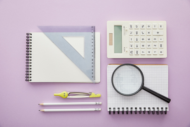 felső nézet nagyító és vonalzó háromszög notebook közelében számológép és írószer elszigetelt lila  - Fotó, kép