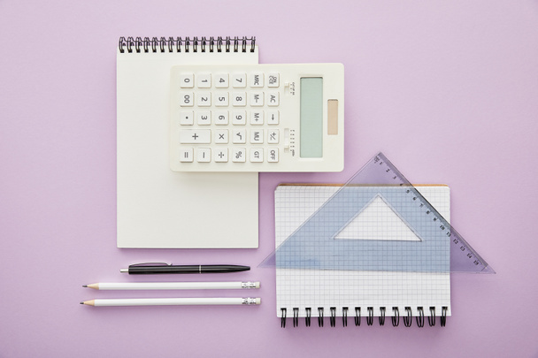 top view of ruler triangle on notebook near calculator and stationery isolated on purple  - Φωτογραφία, εικόνα
