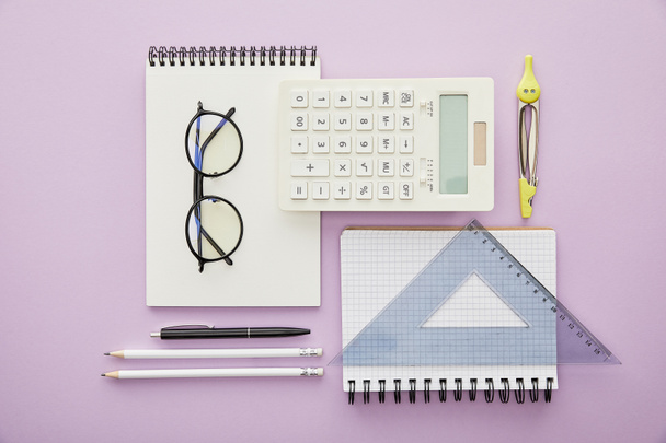 płaska leżanka z linijkami i kalkulatorem w pobliżu notebooków i artykułów piśmiennych izolowanych na fioletowo  - Zdjęcie, obraz
