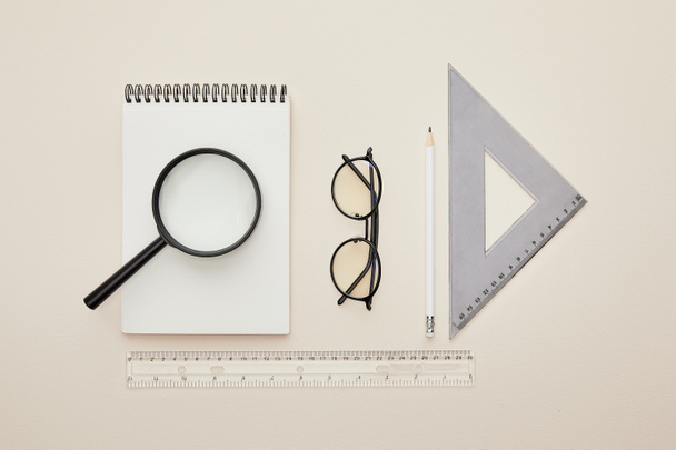top view of magnifier on notebook near glasses and rulers isolated on beige  - Foto, immagini
