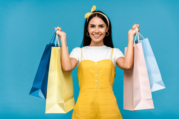 happy young woman holding colorful shopping bags isolated on blue  - Zdjęcie, obraz