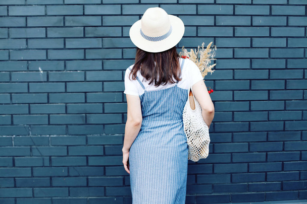 Rear view of woman in denim dress holding knitted bag with goods - Photo, Image