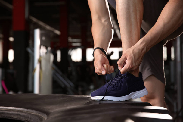 Спортивный молодой человек завязывает шнурки в спортзале
 - Фото, изображение