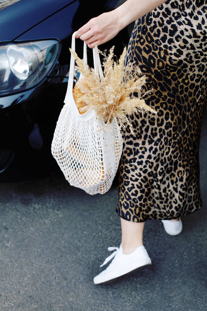 junge Frau im Leopardenkleid trägt Stricktasche mit Waren im Auto - Foto, Bild