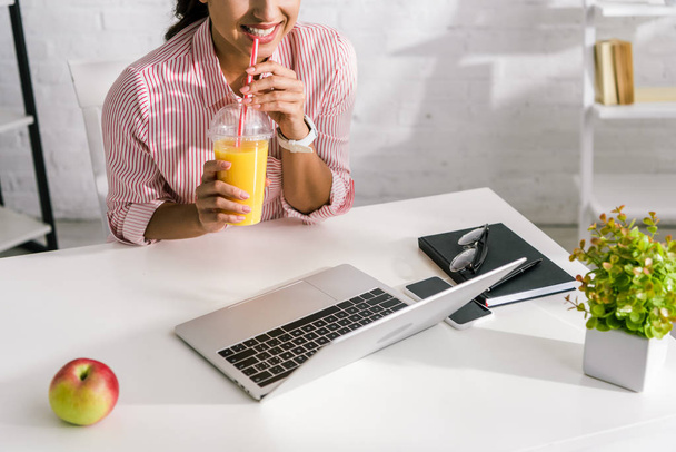 cropped view of girl holding orange juice near laptop  - Foto, Bild