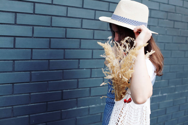 Young woman in hat, denim dress walking with knitted bag with wheat - Foto, Bild