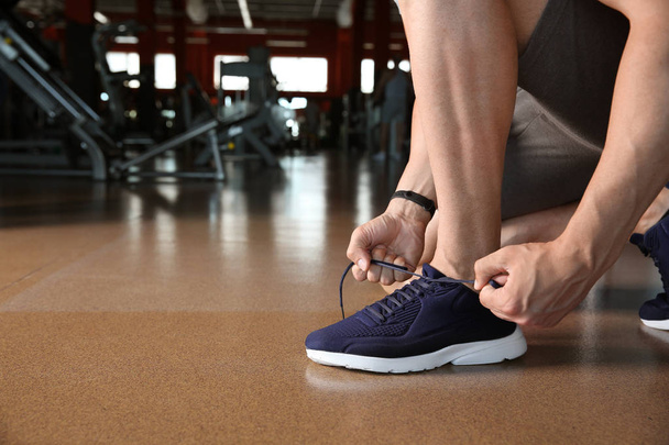 Sporty young man tying shoelaces in gym - Zdjęcie, obraz