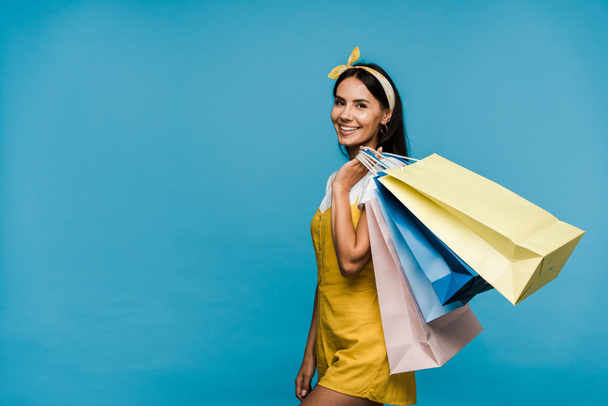 onnellinen nuori nainen seisoo värikkäitä ostoskasseja eristetty sininen
  - Valokuva, kuva