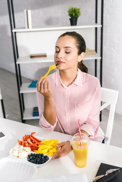 aantrekkelijke vrouw met gesloten ogen houden plastic vork met paprika  - Foto, afbeelding