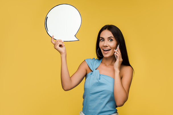 happy girl holding blank speech bubble while talking on smartphone isolated on orange  - Foto, immagini
