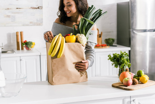 happy girl looking at tasty bananas in paper bag  - Фото, зображення