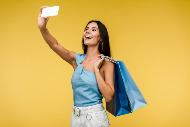 Szczęśliwa kobieta trzyma torby na zakupy i robienia selfie na smartfonie na pomarańczowo  - Zdjęcie, obraz