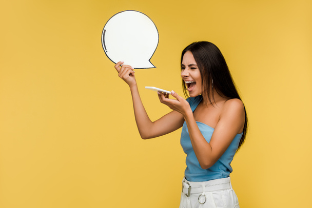 emotional girl holding blank speech bubble and screaming while using smartphone isolated on orange  - Fotografie, Obrázek