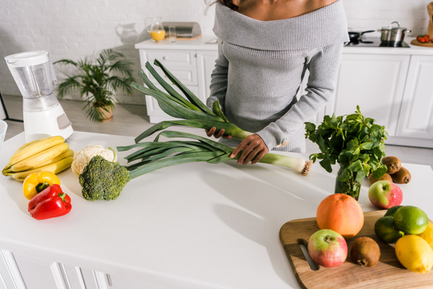 vista recortada de niña sosteniendo puerro cerca de verduras y frutas en la mesa
  - Foto, Imagen