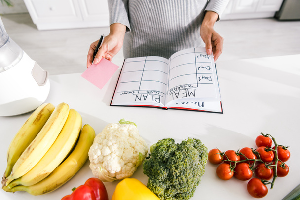обрезанный вид женщины рядом с ноутбуком с планом питания и овощами на столе
  - Фото, изображение