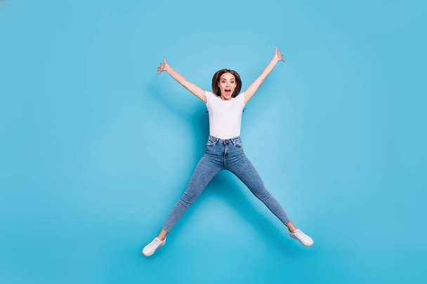 Full size photo of cheerful youth raising hands shouting wearing white t-shirt denim jeans isolated over blue background - Photo, Image