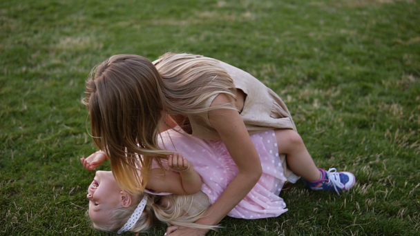 Jeune mère blonde et petite fille mignonne s'amusent à l'extérieur, jouant ensemble dans un parc verdoyant. Bébé couché sur les jambes de la mère et rire pendant qu'elle chatouille, au ralenti. Images grand angle
 - Séquence, vidéo