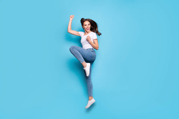 Full size photo of cheerful teen raising fists screaming yeah wearing white t-shirt denim jeans sneakers isolated over blue background - Zdjęcie, obraz