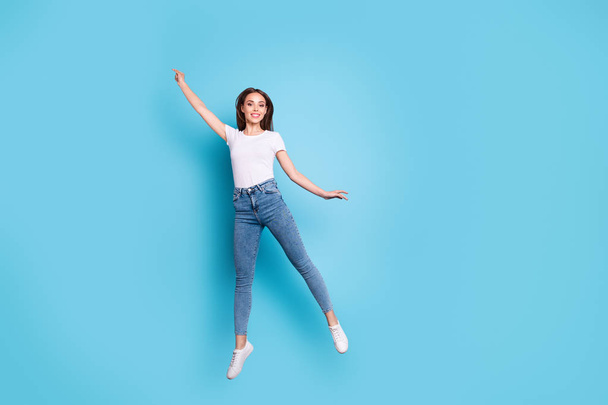 Full body photo of cute youngster raising arms up wearing white t-shirt denim jeans sneakers isolated over blue background - Photo, image