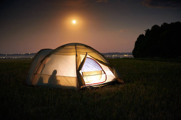 Reizen en kamperen concept-Camp tent 's nachts onder een hemel vol sterren. Oranje verlichte tent met een persoon binnenin. Prachtige natuur-veld, bos, vlakte. Moon en Moonlight - Foto, afbeelding