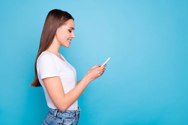 Profile side photo of cute lady looking into her device smiling searching news wearing white t-shirt denim isolated over blue background - Фото, изображение